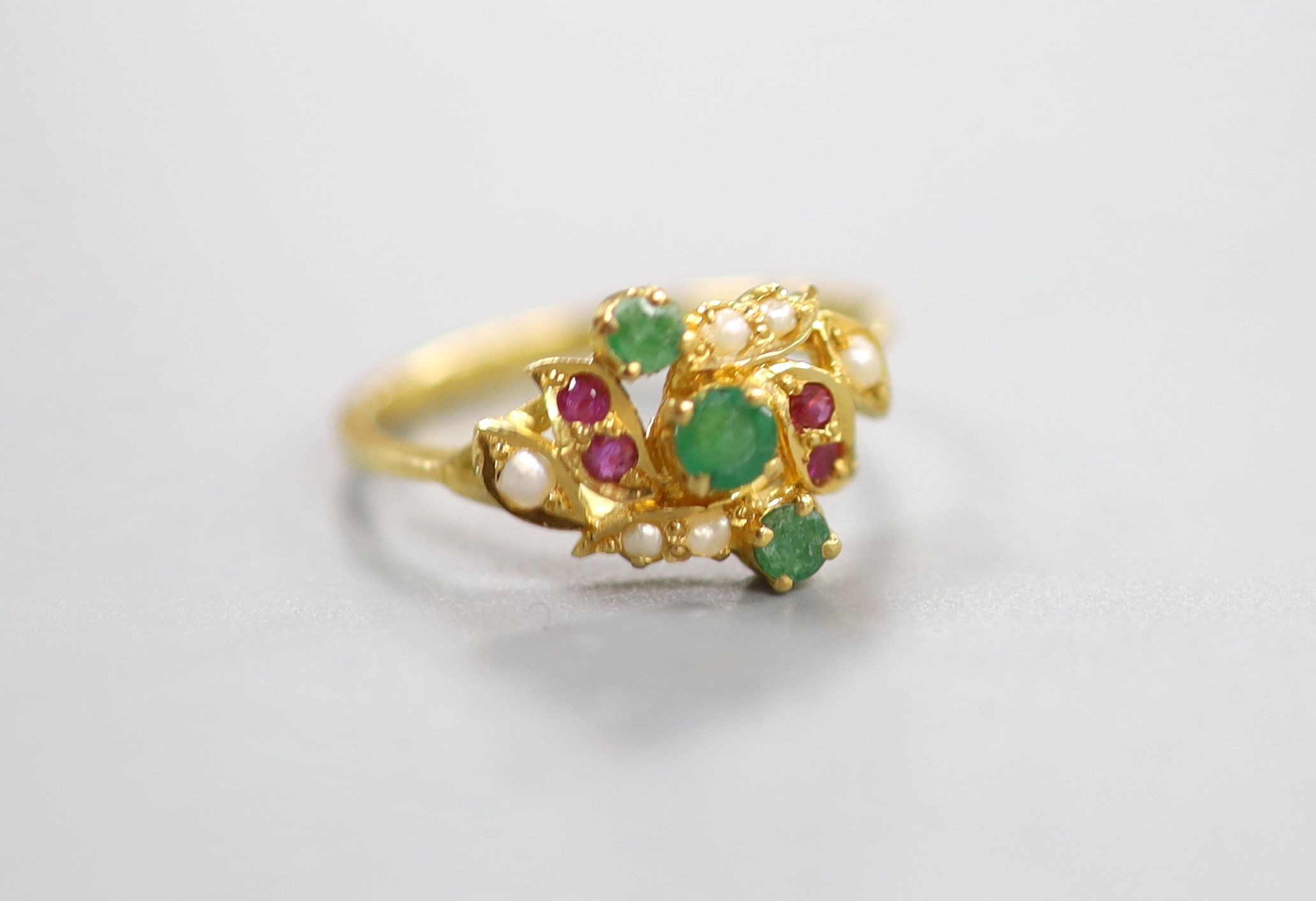 A modern yellow metal, emerald, ruby and seed pearl cluster set crossover ring, size L, gross weight 2.9 grams.